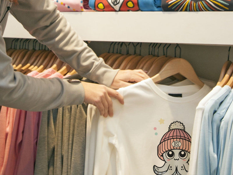 Person holding a white sweatshirt with a cartoon design in a clothing store.