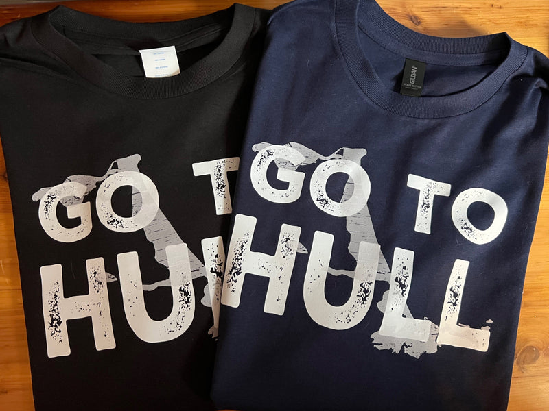 Two t-shirts with text 'GO TO HULL' on a wooden surface