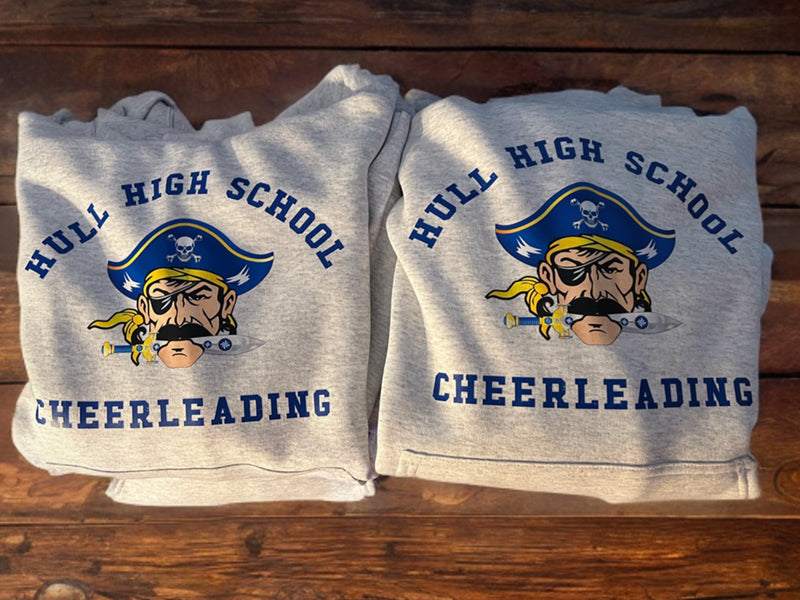 Folded sweatshirts with 'Hull High School Cheerleading' design on a wooden surface