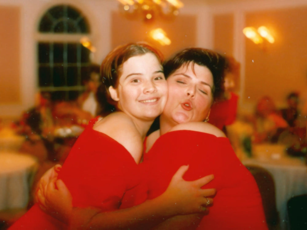 Two women in red dresses hugging in a festive indoor setting with blurred background