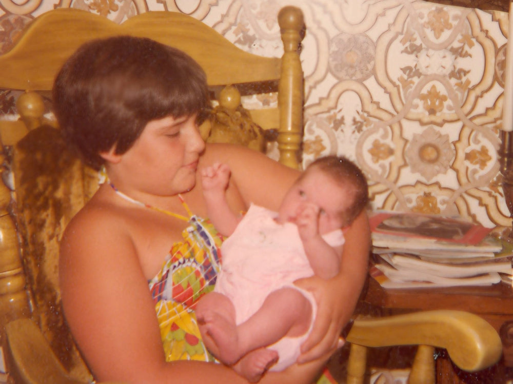 Person holding a baby in a room with patterned wallpaper