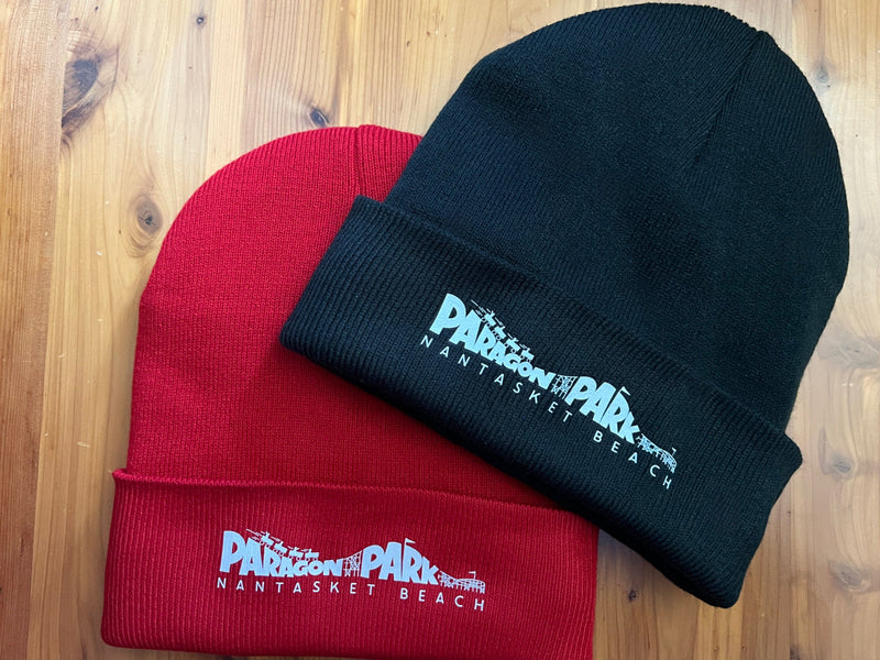 Two beanies, one red and one black, with a logo on a wooden surface.