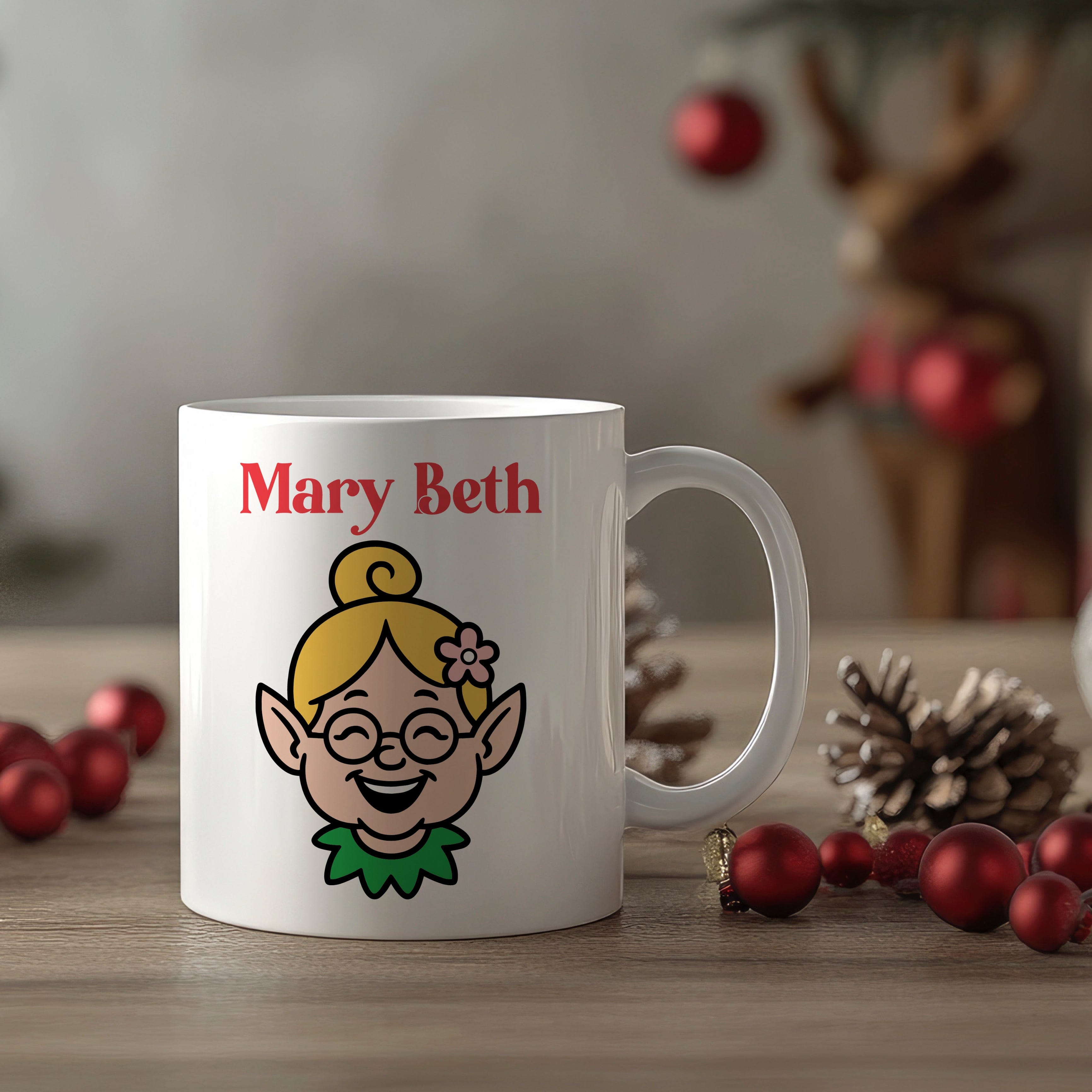 White mug with an elf design and 'Mary Beth' text, surrounded by Christmas decorations.