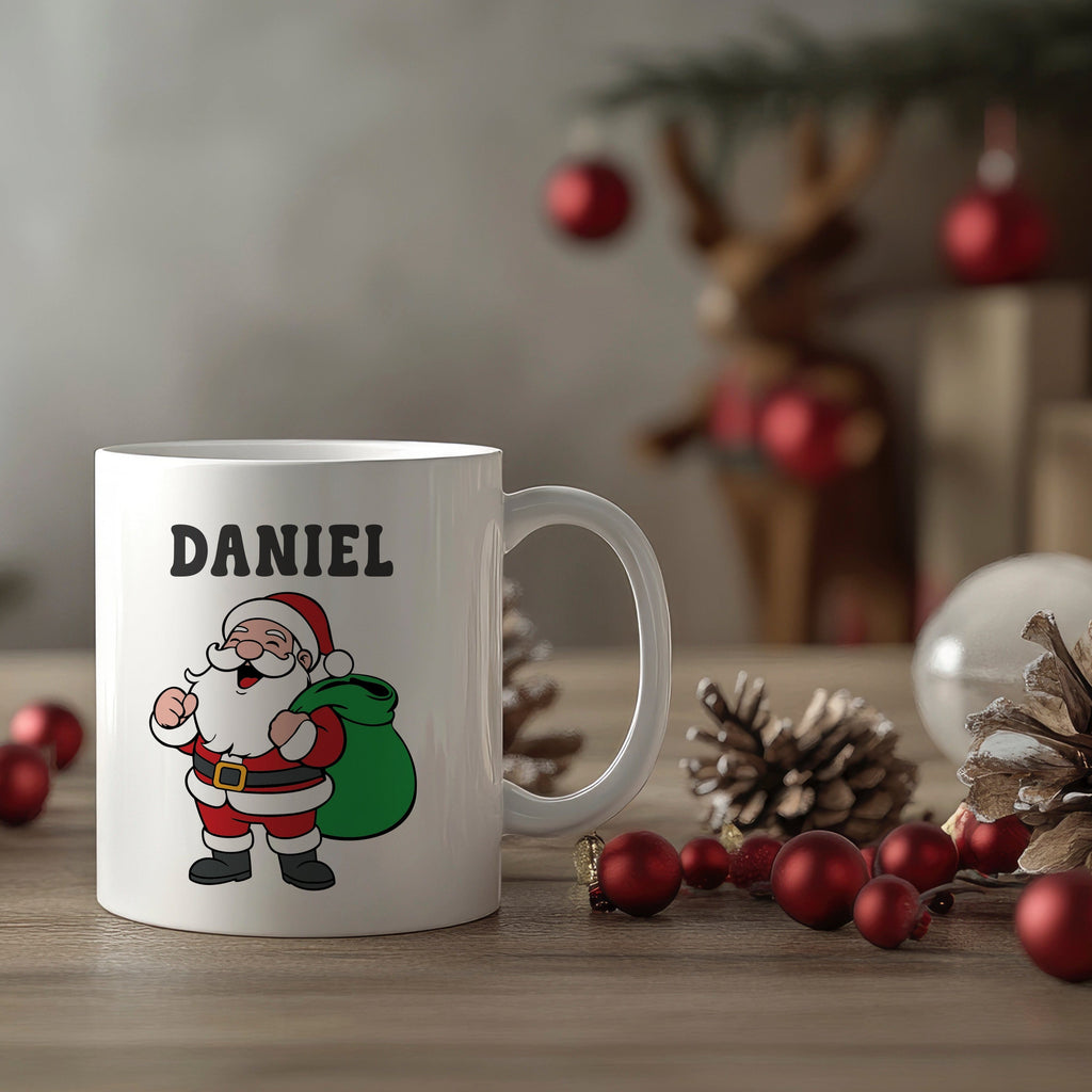 White mug with a cartoon Santa Claus design and 'DANIEL' text, placed on a wooden surface with Christmas decorations.
