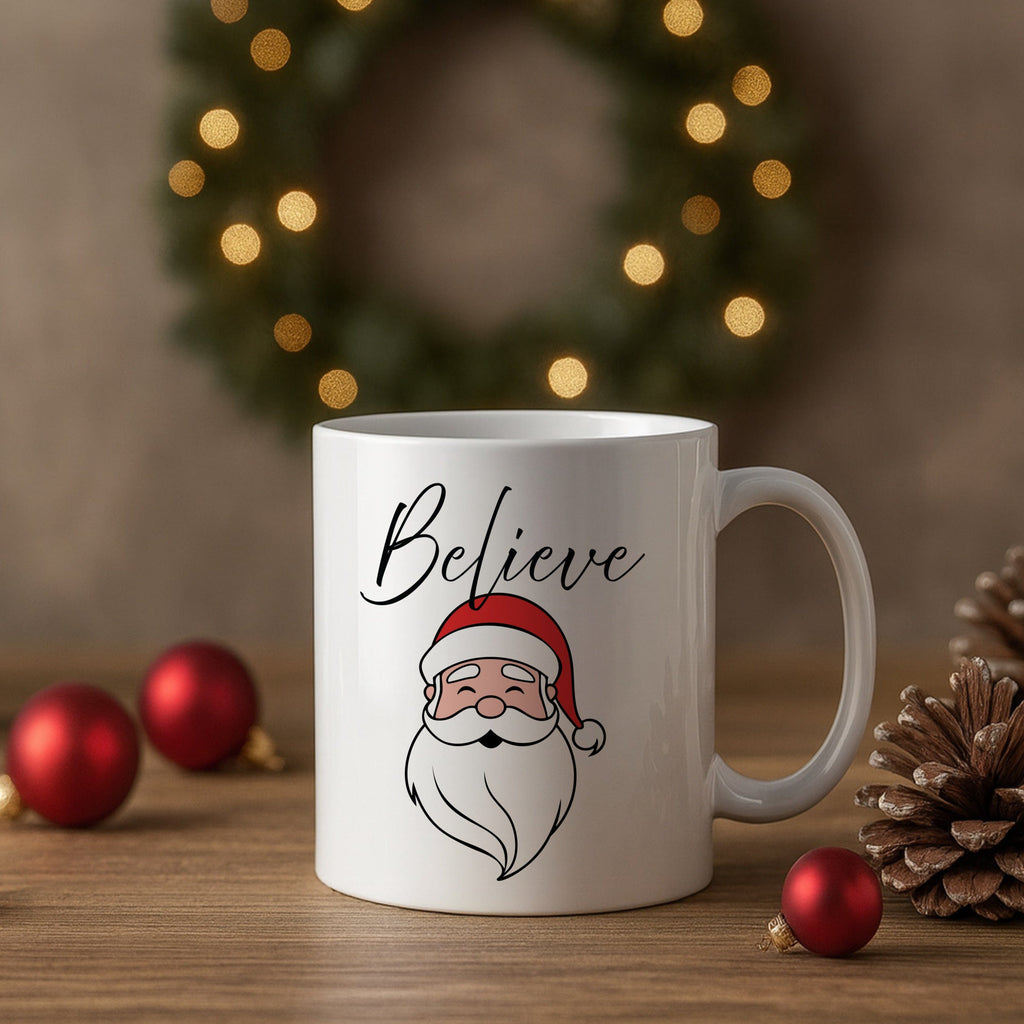 White mug with Santa Claus illustration and 'Believe' text, placed on a wooden surface with Christmas decorations.