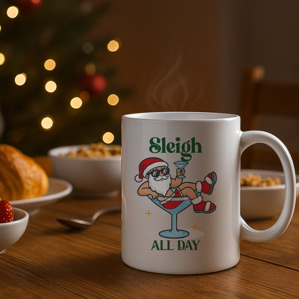 White mug with Santa Claus design and 'Sleigh All Day' text on a table with food and Christmas lights in the background.