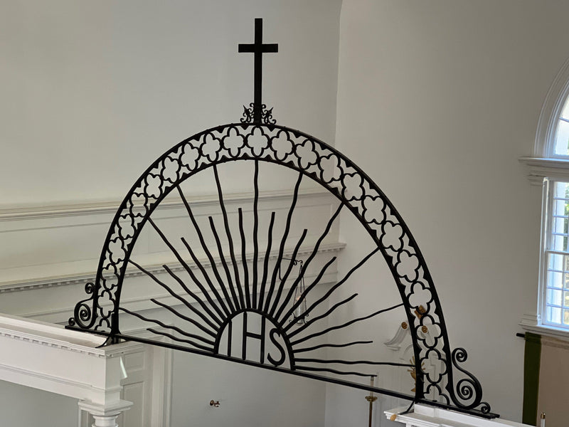 Decorative metal arch with 'HPS' initials and cross on a white wall.