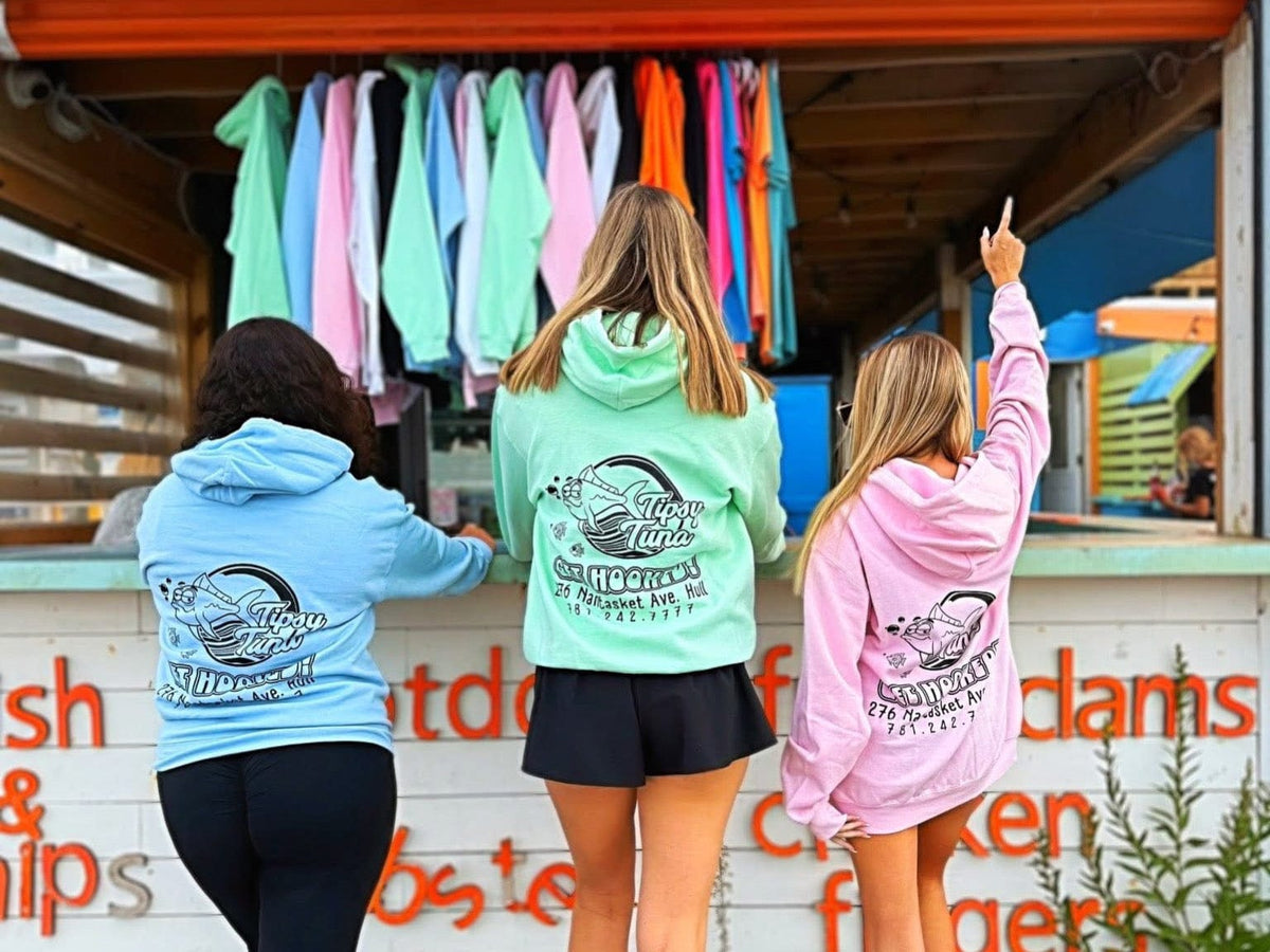 Three people wearing colorful hoodies in front of a food truck with clothes hanging above.