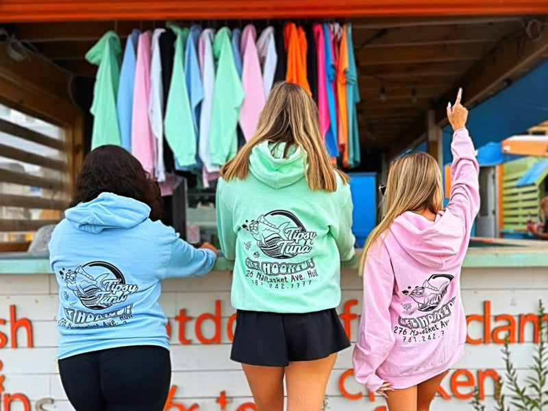 Three people wearing hoodies with a logo in front of a clothing stall.